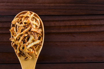 Fresh homemade crispy fried onion strings on wooden spoon, photographed overhead with copy space on...