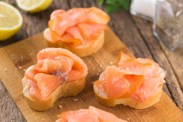 Smoked salmon slices on baguette on wooden board (Selective Focus, Focus one third into the image)