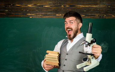 Happy student with books and microscope near blackboard with copy space. Education, school, teaching. Biology or chemistry science. Positive teacher with books and microscope. Student in auditorium.