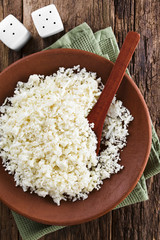Freshly grated raw cauliflower rice on plate with wooden spoon, photographed overhead