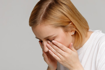 Fototapeta premium Close up of young woman has a problem with contact lenses, rubbing her swollen eyes due to pollen, dust allergy. Dry eye syndrome, watery, itching. Isolated on grey background, free space. 