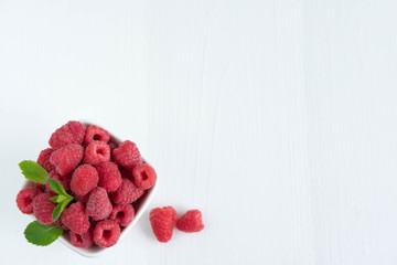 Raspberry berries in a white plate on a light wooden background. Useful berries for health. Photo of raspberry with space for copisapase