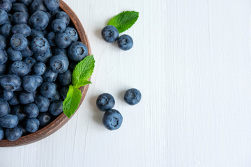 Closeup of blueberry berries with mint leaves in a clay plate on a light wooden background. Photo of blueberry for designers on the banner. Useful berries for sight