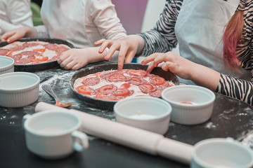 close up. a little girl lays out pieces of tomatoes on the basis of pizza.