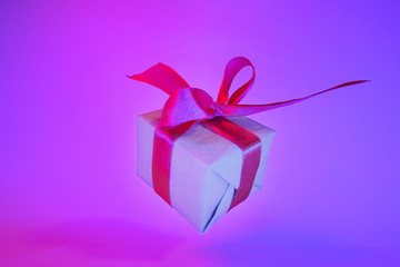 Gift box with red ribbon on trendy neon color background. zero gravity. levitation. copyspace. Concept sales, discount price, christmas presents and shopping