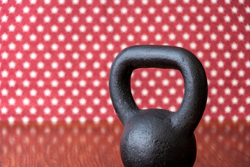 Naklejka na ściany i meble Rustic black kettlebell on a wood floor against a patterned backdrop of red and white