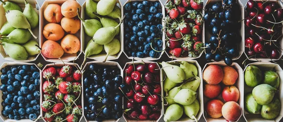 Selbstklebende Fototapeten Summer fruit and berry variety. Flat-lay of ripe strawberries, cherries, grapes, blueberries, pears, apricots, figs in wooden eco-friendly boxes over grey background, top view © sonyakamoz