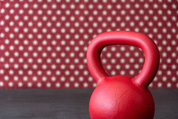 Naklejka na ściany i meble Large red kettlebell on a black rubber mat floor against a patterned backdrop of red and white