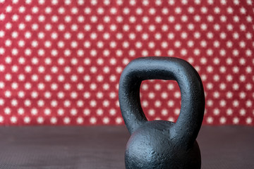 Naklejka na ściany i meble Rustic black kettlebell on a black rubber mat floor against a patterned backdrop of red and white