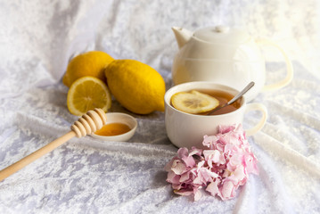 Cup of tea and teapot with lemons and honey on a white background, pink hortensia and a cup of tea, close up
