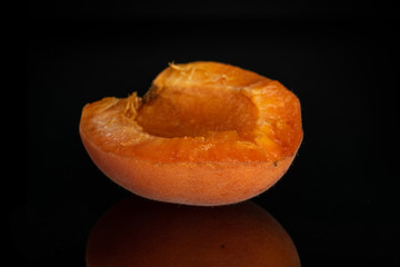 One half of meaty fresh deep orange apricot isolated on black glass