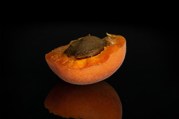 One half of fresh deep orange apricot with a stone isolated on black glass