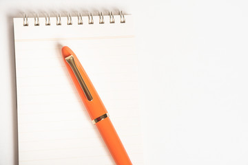 A shiny orange fountain pen together with a spiral-bound notebook.