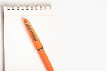 A shiny orange fountain pen together with a spiral-bound notebook.