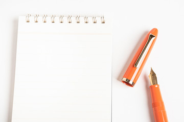 A shiny orange fountain pen together with a spiral-bound notebook.