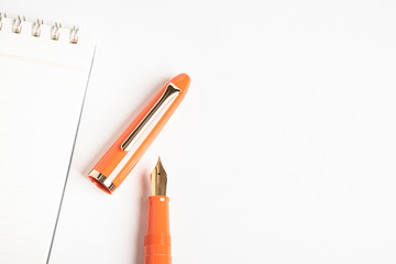 A shiny orange fountain pen together with a spiral-bound notebook.