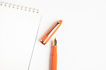 A shiny orange fountain pen together with a spiral-bound notebook.