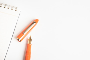 A shiny orange fountain pen together with a spiral-bound notebook.