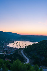 Fototapeta na wymiar Landscape and top view of the old historic city of Vis and the harbor with moored sailing boats and yachts during a beautiful sunset in summer, Vis island, Croatia, Europe
