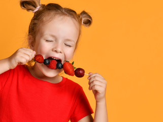 Baby girl kid in red t-shirt holding smelling biting eating fresh berries dessert with cherry...