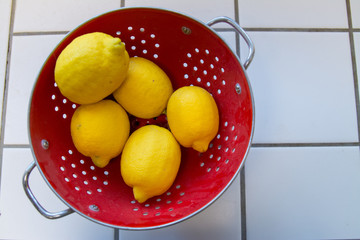 Large ripe lemons in a red colander.