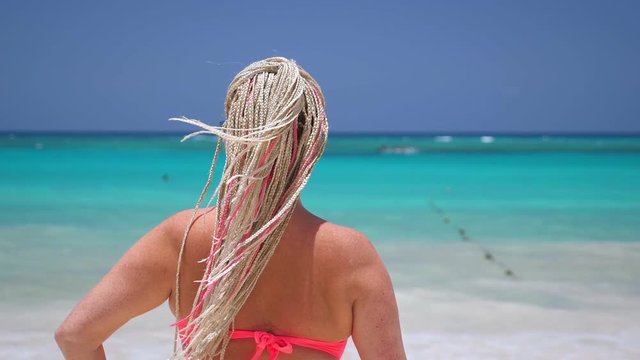 Woman with african braids in pink bikini on tropical beach with turquoise sea water. Travel destinations. Summer vacations
