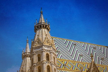 Fototapeta na wymiar Aerial view over the rooftops St. Stephen's Cathedral including the cathedral's famous ornately patterned, multi colored roof with blue sky , Austria