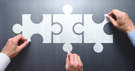 Finding solution of business relationship. Successful business team concept. Businessmen drawing puzzle pieces on chalkboard.