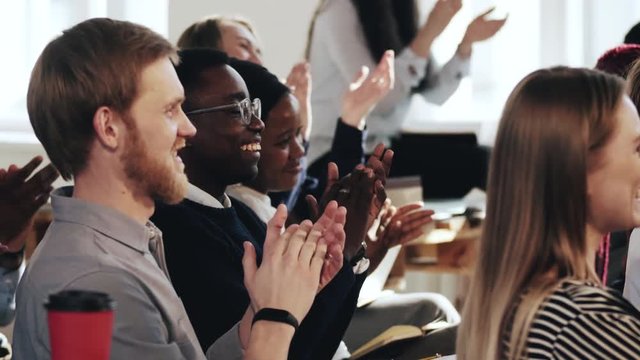 Side view close-up happy smiling young multiethnic audience clapping to speaker at modern office training seminar event.