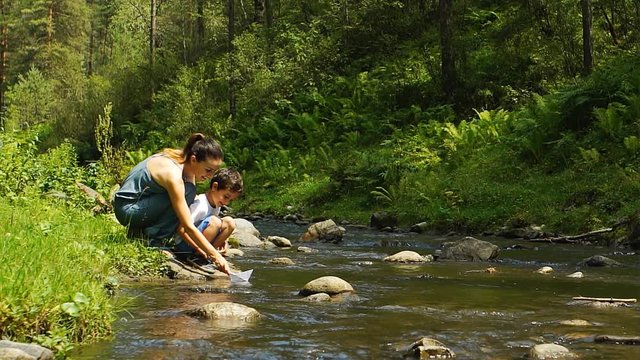 Pretty Mother And Her Son Playing With A Paper Ship At The Mountain Stream