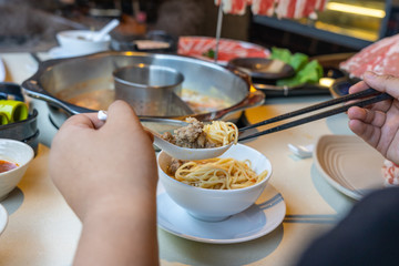 Woman hands using chopsticks and spoon while eating hotpot