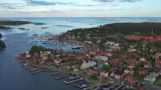 Sandhamn islands colourful marina residence rooftops, tilt down view over sailboats on coastal harbour.
