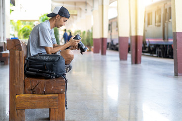 Asian man Traveler with check the image file from the camera and backpack, at train station in Thailand
