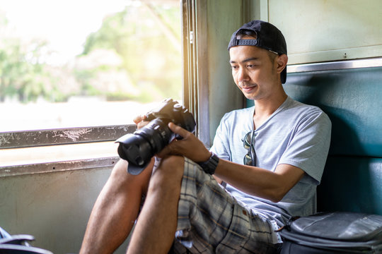 Asian man Traveler with hand holding photo camera and backpack, Sit on the old train seat at Thailand