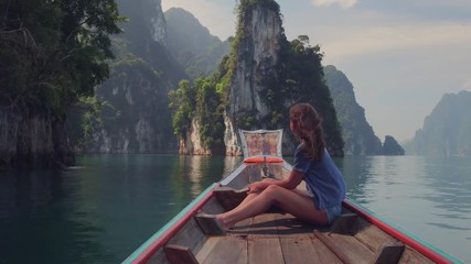 Lifestyle video of pretty travel woman sitting in wood long tail boat on tropical limestone cliffs . Explore and vacation concept. Khao Sok lake, Thailand.