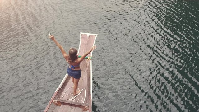 AERIAL. Happy girl stand on board of sailing boat have fun discovering islands in tropical sea on summer coastal cruise.