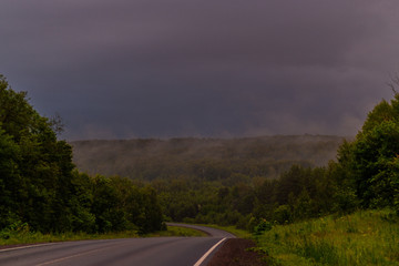 Wet asphalt after rain. Thick rain clouds. The road along the forest. Ural Mountains in rainy summer weather