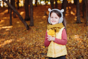 Autumn season. Portrait of happy cute girl standing with bunch of yellow maple leaves in forest. Foliage background.