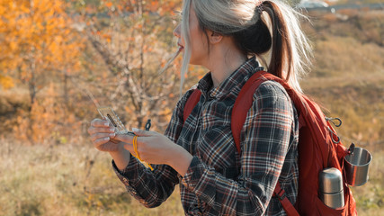 Hiking tourism. Side view of lady with backpack using compass to explore country. Fall landscape background.