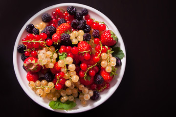 Healthy mixed berry with strawberry, blackberry, red and white currant on the black background. Top view. Copy space.