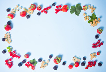 Colorful frame made with blackberry, strawberry, red and white currant on the blue background. Flat lay. Top view.
