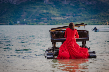 woman dressed in red playing the piano on a lake