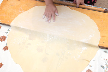 Hands working with bread dough recipe preparation. Female hands making dough. Women's hands roll out the dough. Mom rolls dough on a kitchen board with a rolling pin