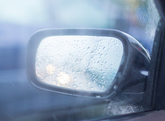 Car side mirror glass with water droplets from rain - driver's side rear view on rainy day