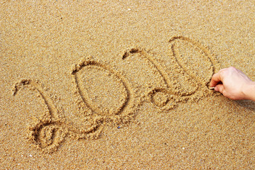 Male hand draws on sand 2020 year, top view