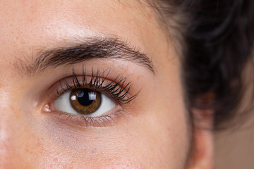 An extreme closeup view on the bright eye of a beautiful Caucasian girl. With brown iris and long lashes. Looking straight into the lens.