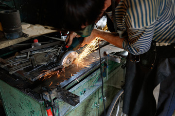 Professional blacksmith sawing metal with hand circular saw at forge.