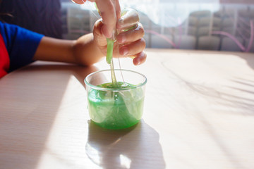 The child plays with toffee a slime of green color. Hands close up