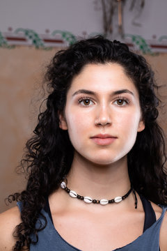 Portrait Of A Beautiful Young Caucasian Girl Looking Straight Into The Camera, With Pale Complexion And Black Hair With Tight Curls. She Wears A Beaded Necklace And Nose Ring.