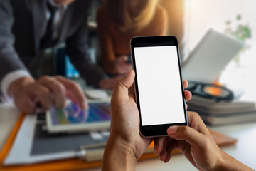 Hand holding white mobile phone with blank white screen  in office.
